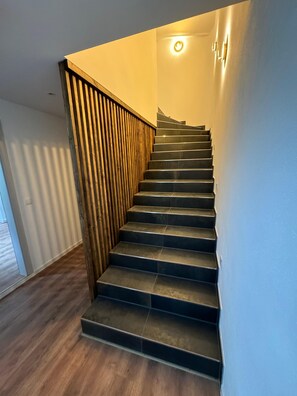 Stairs lead up to a light fixture, flanked by a railing and a wall.