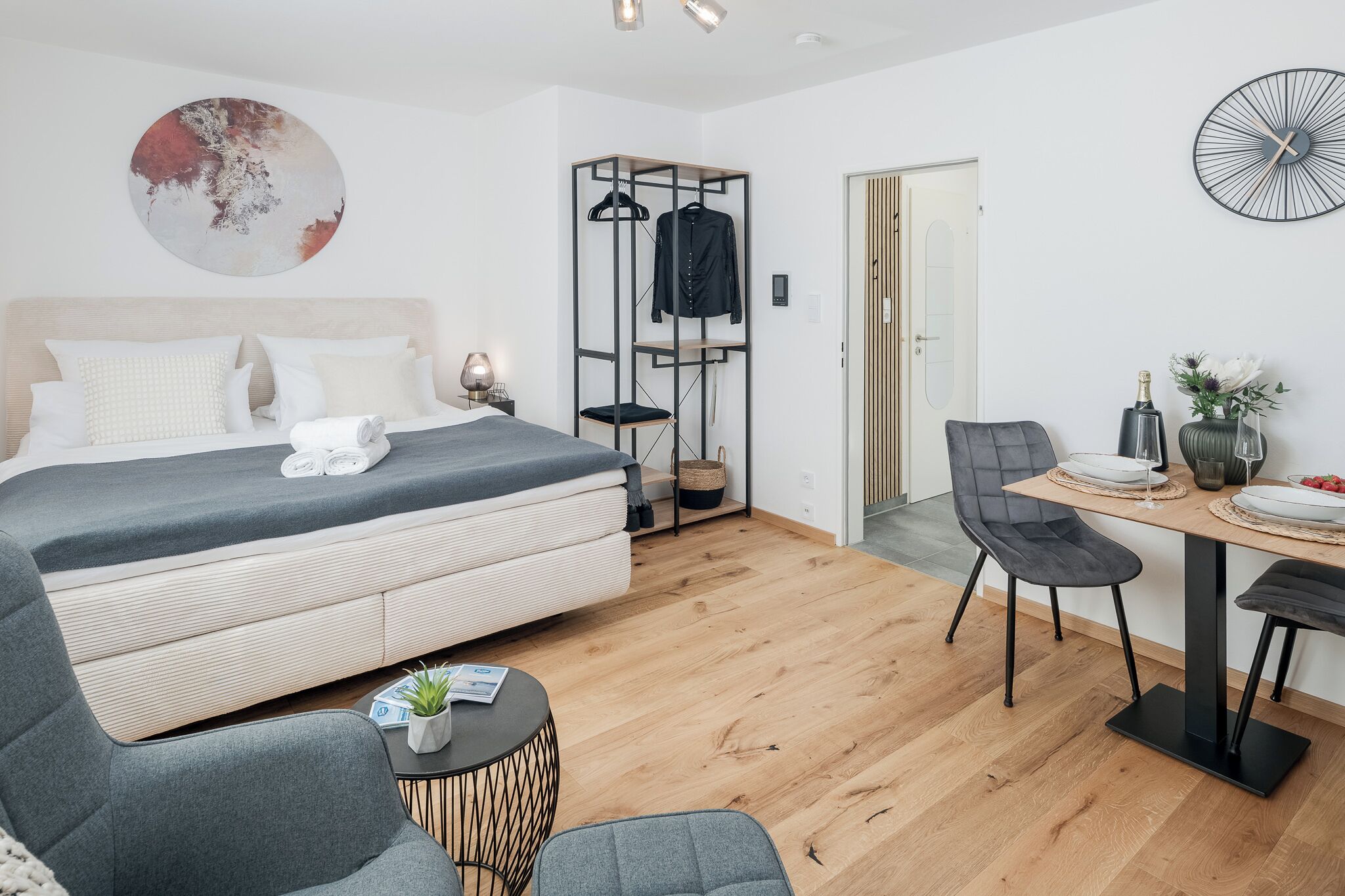 Una habitación de hotel moderna con una cama, un rincón de estar con una mesa y sillas, un armario y una mesa de comedor para dos.