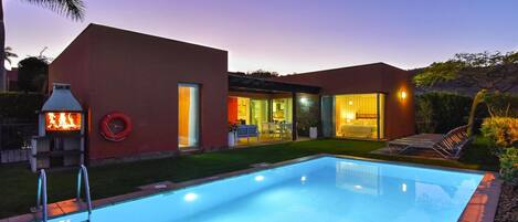 A modern house with a swimming pool, a barbecue area, and a patio with outdoor furniture.