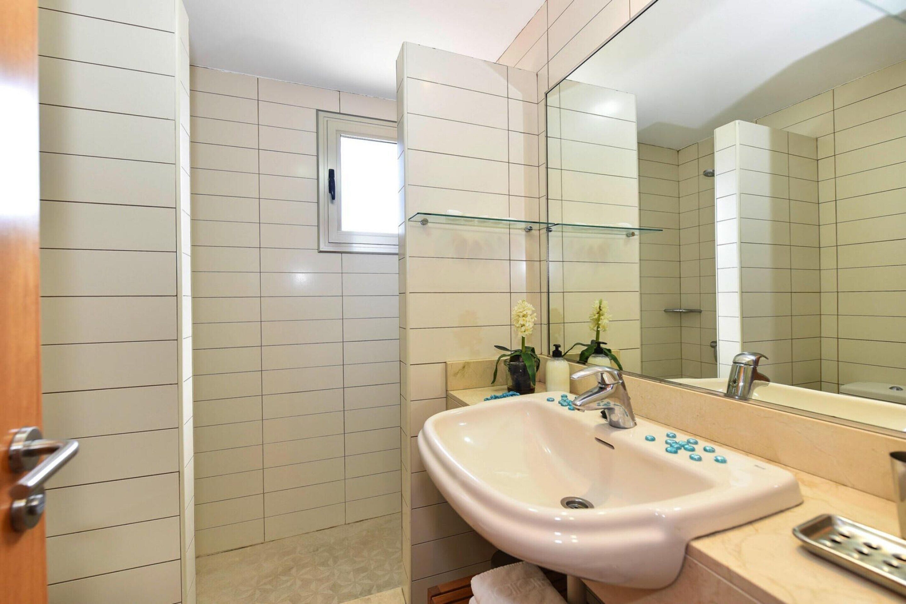 A bathroom with a white sink, a glass shelf, and a mirror.