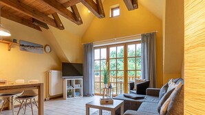 A cozy living room with a sofa, a TV, and a dining area with chairs and a table. - Landhaus in Vollerwiek (Vollerwiek)