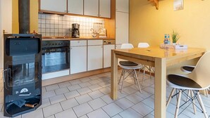 A kitchen with a stove, oven, and white cabinets. There is a dining table with chairs and a hanging light fixture. - Landhaus in Vollerwiek (Vollerwiek)
