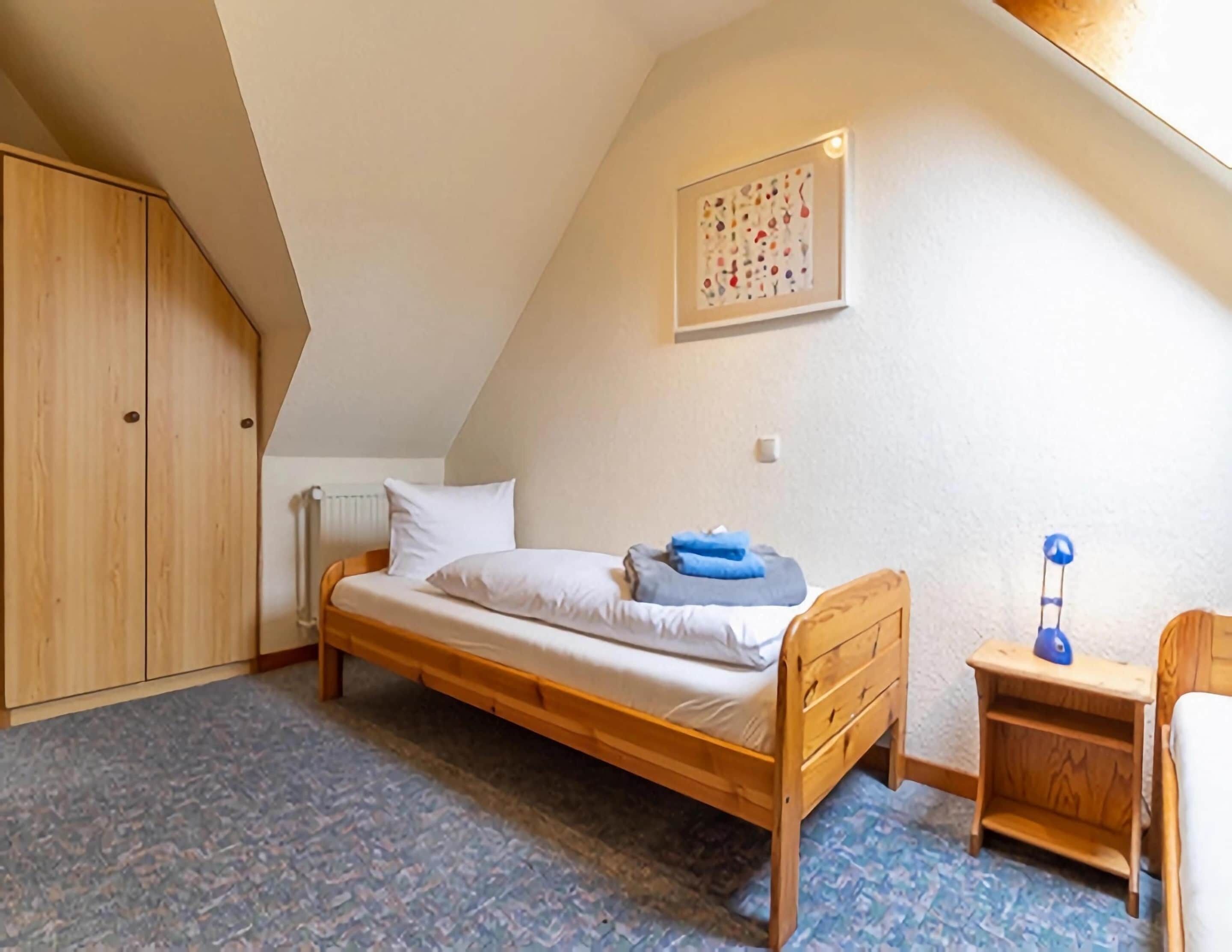 Una habitación pequeña con cama individual, techo inclinado, muebles de madera y un radiador.