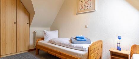 A small, single-bed room with a sloped ceiling, wooden furniture, and a radiator.