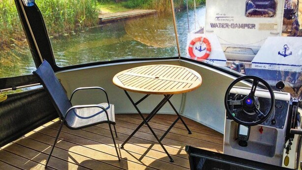 A boat's interior with a steering wheel, a table, and a chair. - Hausboot auf der Peene, Demmin (Demmin)
