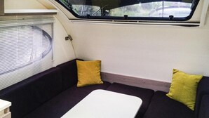 A compact living space with a sofa and a small table, a window with blinds, and a view of the outside. - Hausboot auf der Peene, Demmin (Demmin)
