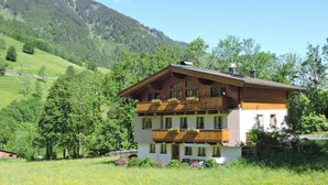 A two-story chalet with wooden balconies, set in a lush green valley with a mountain backdrop. - Apartment in Fusch Near Grossglockner Road (Fusch an der Grossglocknerstrasse)