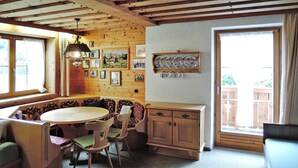 A cozy room with a wooden bench, a round table, and chairs. There is a wooden cabinet and a shelf with dishes. Pictures are hung on the wall. - Apartment in Fusch Near Grossglockner Road (Fusch an der Grossglocknerstrasse)