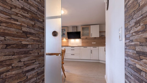 A modern kitchen with white cabinets, a wooden countertop, and a stone wall. - Ferienwohnung fur Familien in St.peter Ording (St. Peter-Ording)