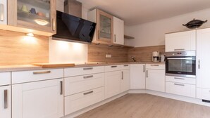 A modern kitchen with white cabinetry, a wooden countertop, a built-in oven, and a coffee maker. - Ferienwohnung fur Familien in St.peter Ording (St. Peter-Ording)