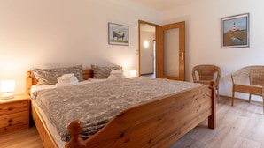 A bedroom with a wooden bed, a nightstand, a chair, and two framed pictures on the wall. - Ferienwohnung fur Familien in St.peter Ording (St. Peter-Ording)
