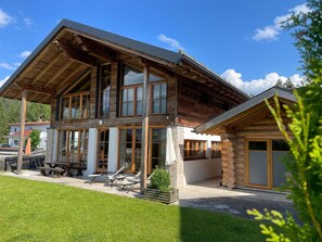 A two-story log cabin with a large porch, stone pillars, and a view of the surrounding area.