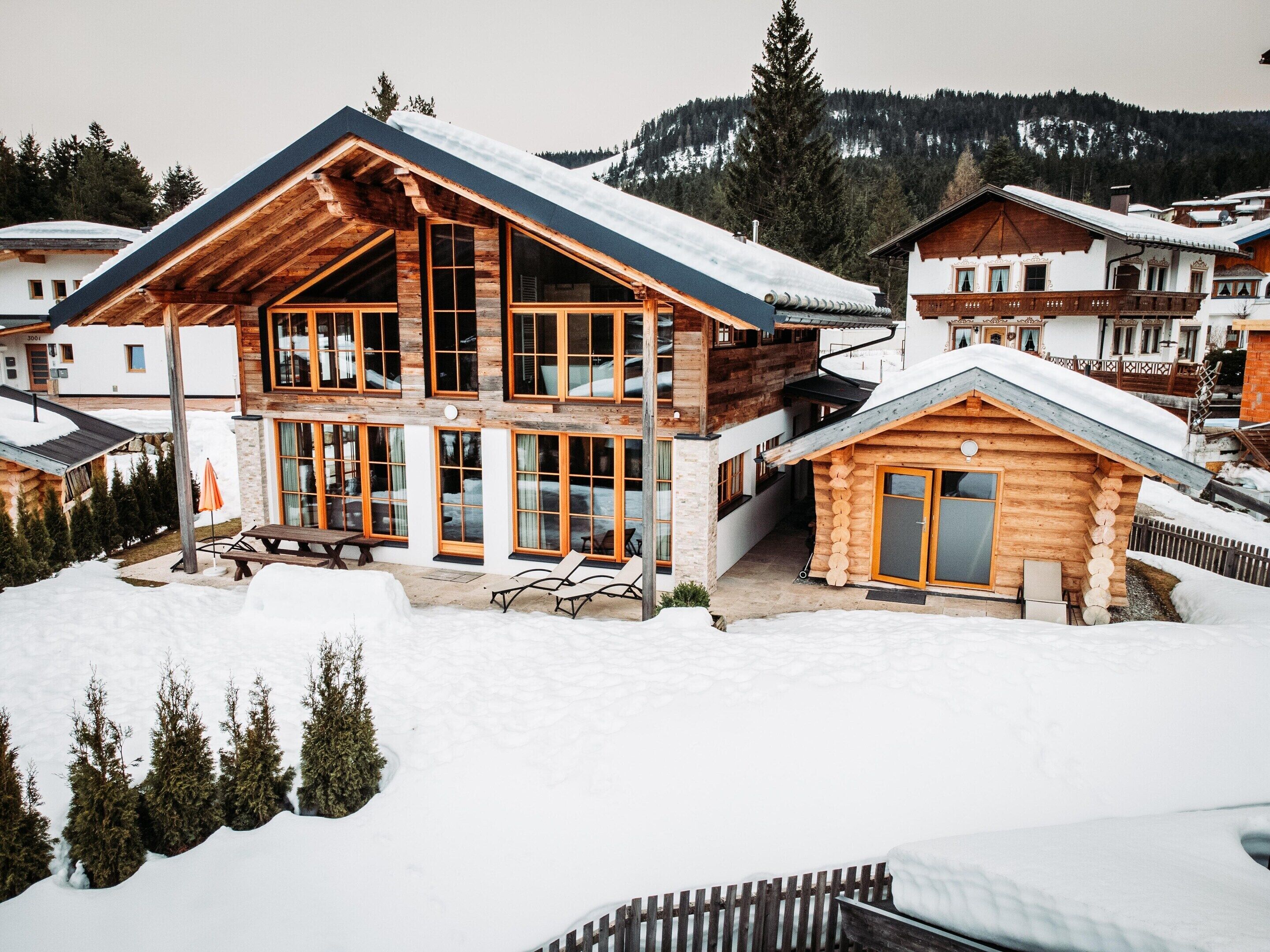 Une cabane en bois à deux étages, dotée de grandes fenêtres et d’un patio couvert.