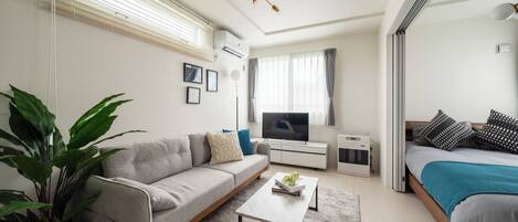A modern living room with a sofa, coffee table, TV, and a bed.