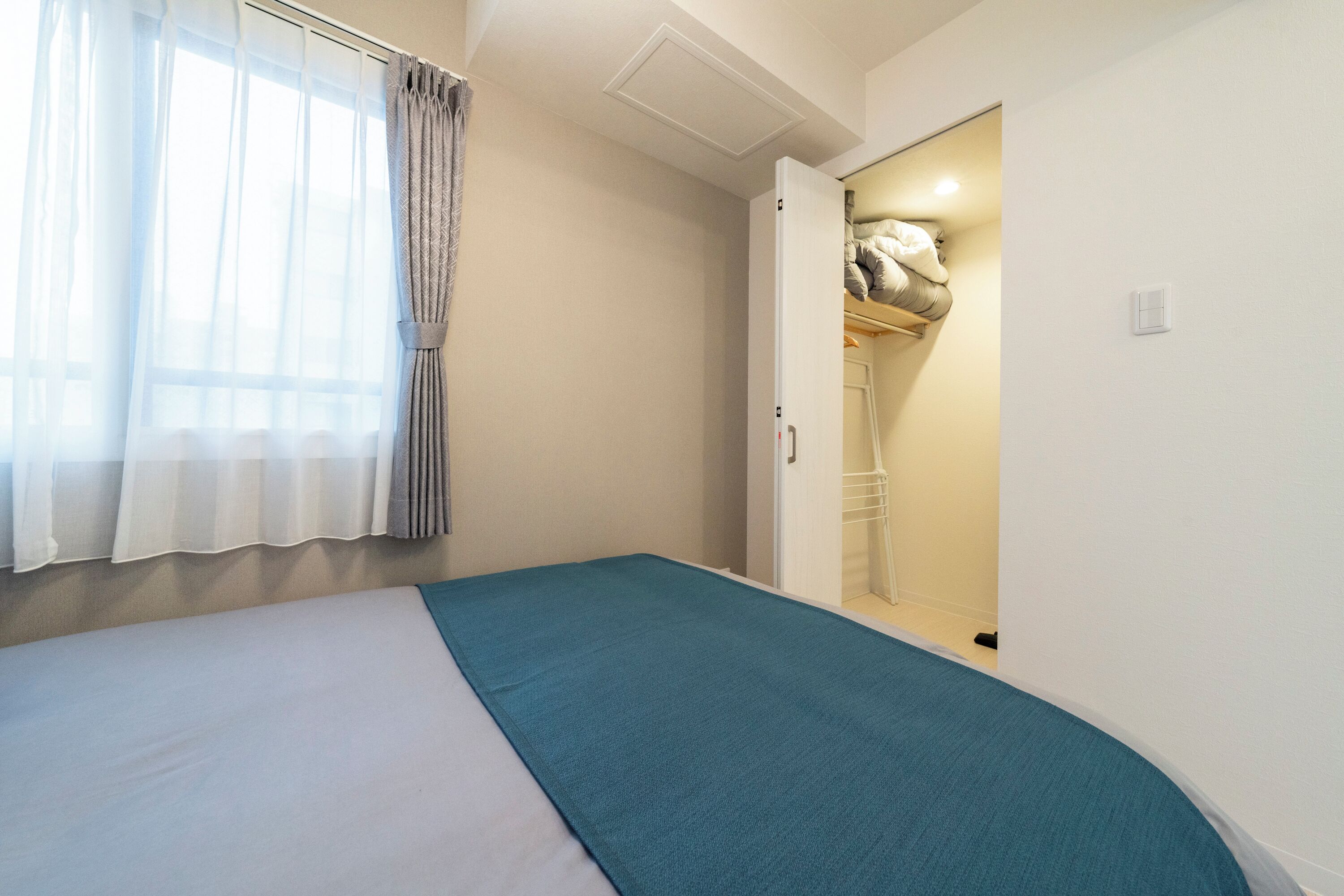 Un dormitorio con cama, ventana con cortinas y armario con perchero.