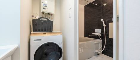 A compact laundry area with a washing machine, a drying rack, and a shower.
