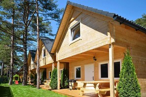 A row of wooden cabins with a covered porch, a picnic table, and a grill. - Chalet in Pobierowo Near Baltic Sea Beach (Rewal)