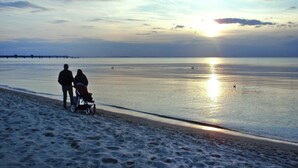 En strandscen med ett lugnt hav, en solnedgång och fotspår i sanden.