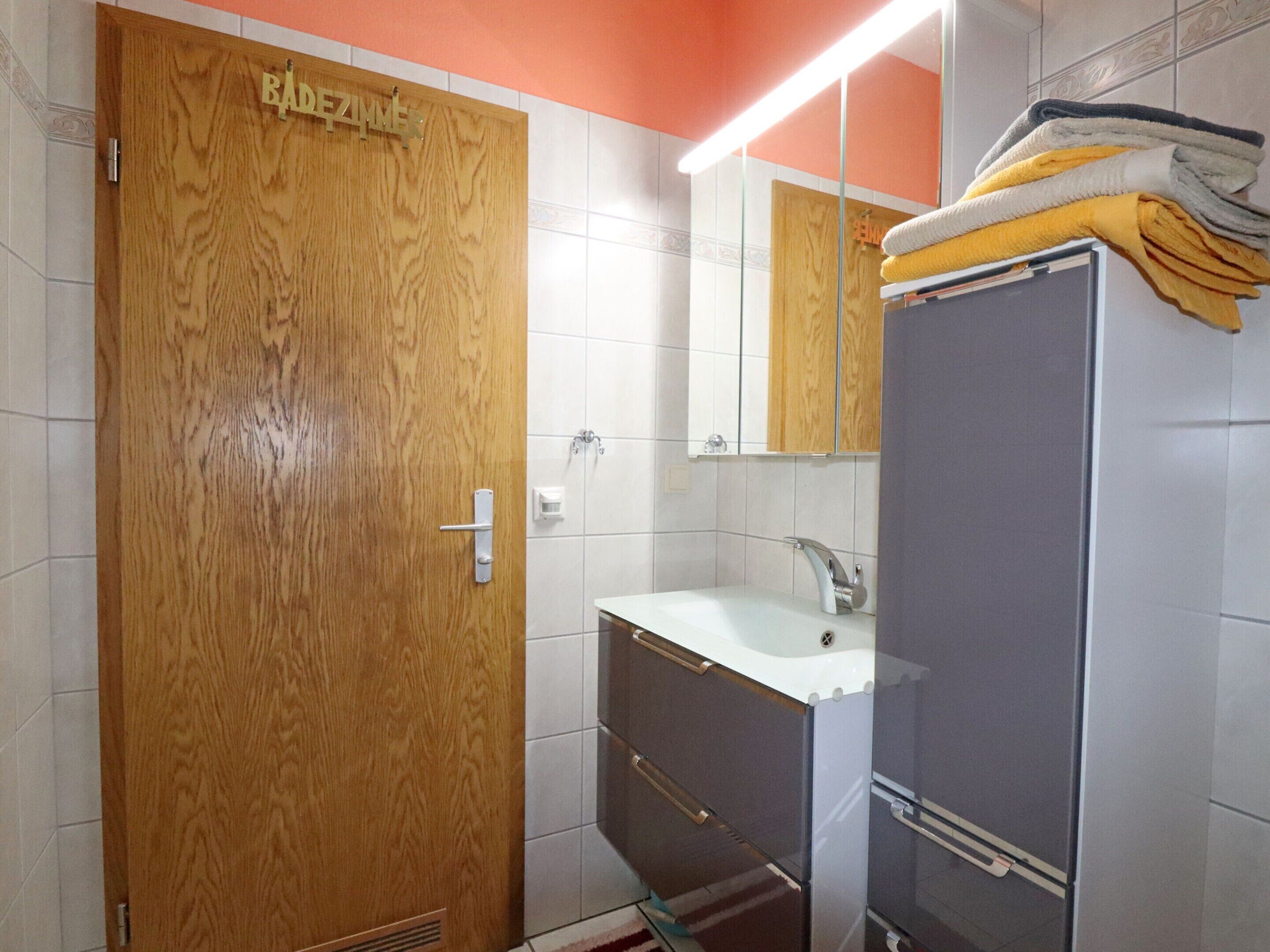 A bathroom with a wooden door, a sink, a mirror, and a towel rack.