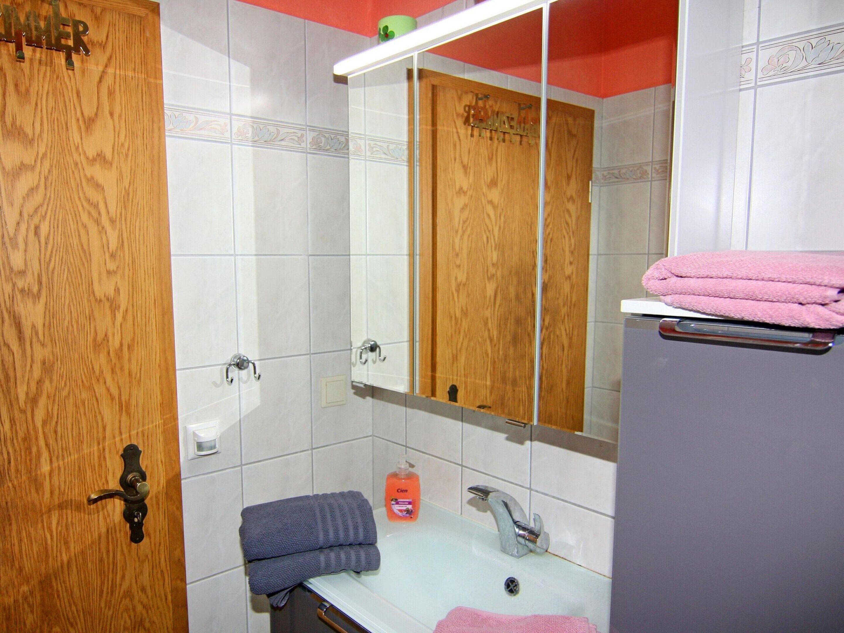 A bathroom with a wooden door, a sink with a mirror above it, and a towel rack with towels.