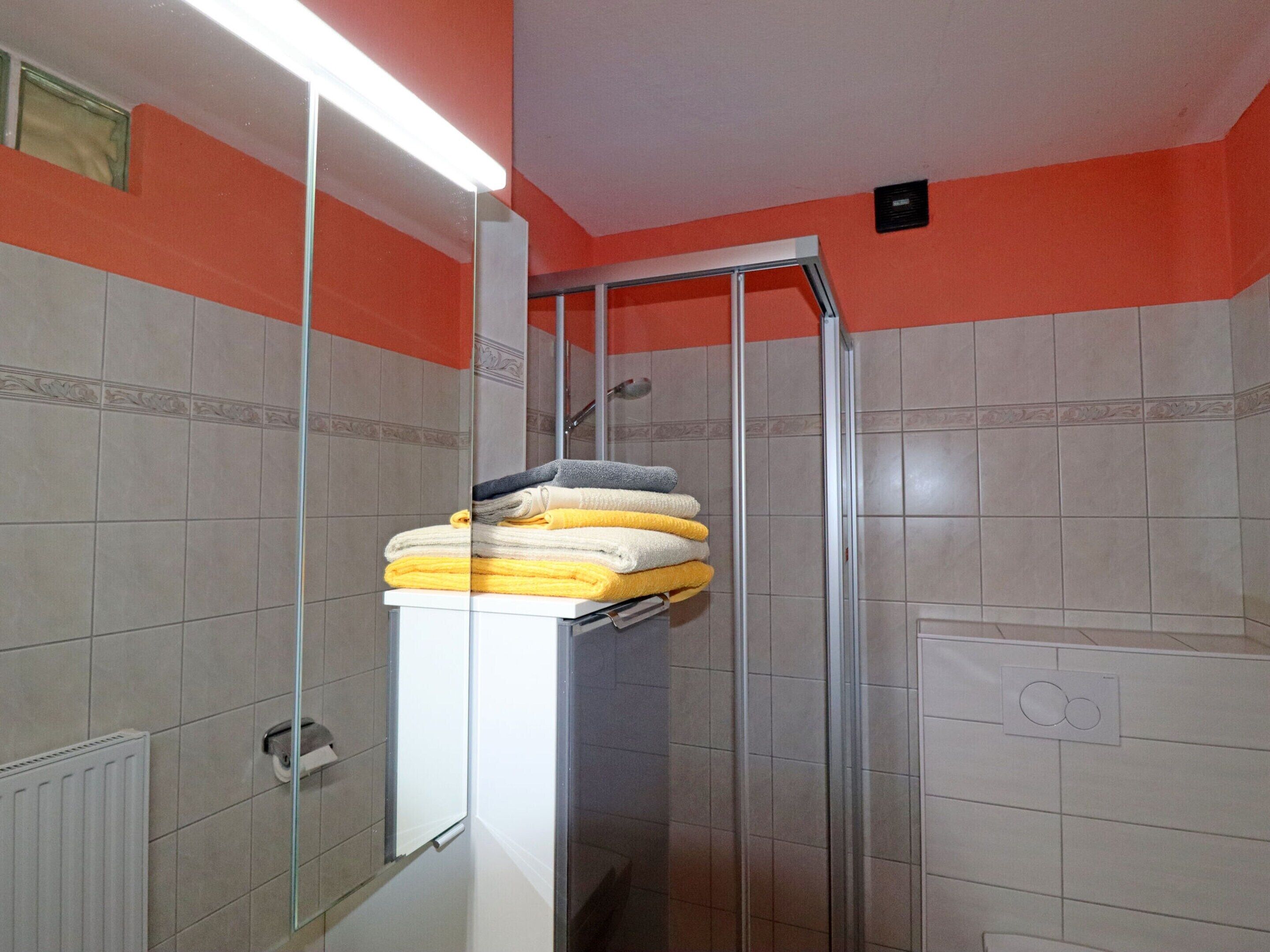 Ein Badezimmer mit Duschkabine aus Glas, einem Stapel Handtüchern und einem weißen Heizkörper.