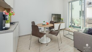 A modern living room with a dining area, a flat-screen TV, and a large window offering a view of the city. - Apartment in Pobierowo Near Baltic Beach (Rewal)