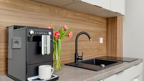 A modern kitchen with a built-in coffee machine, a sink, and a vase with flowers. - Apartment in Pobierowo Near Baltic Beach (Rewal)