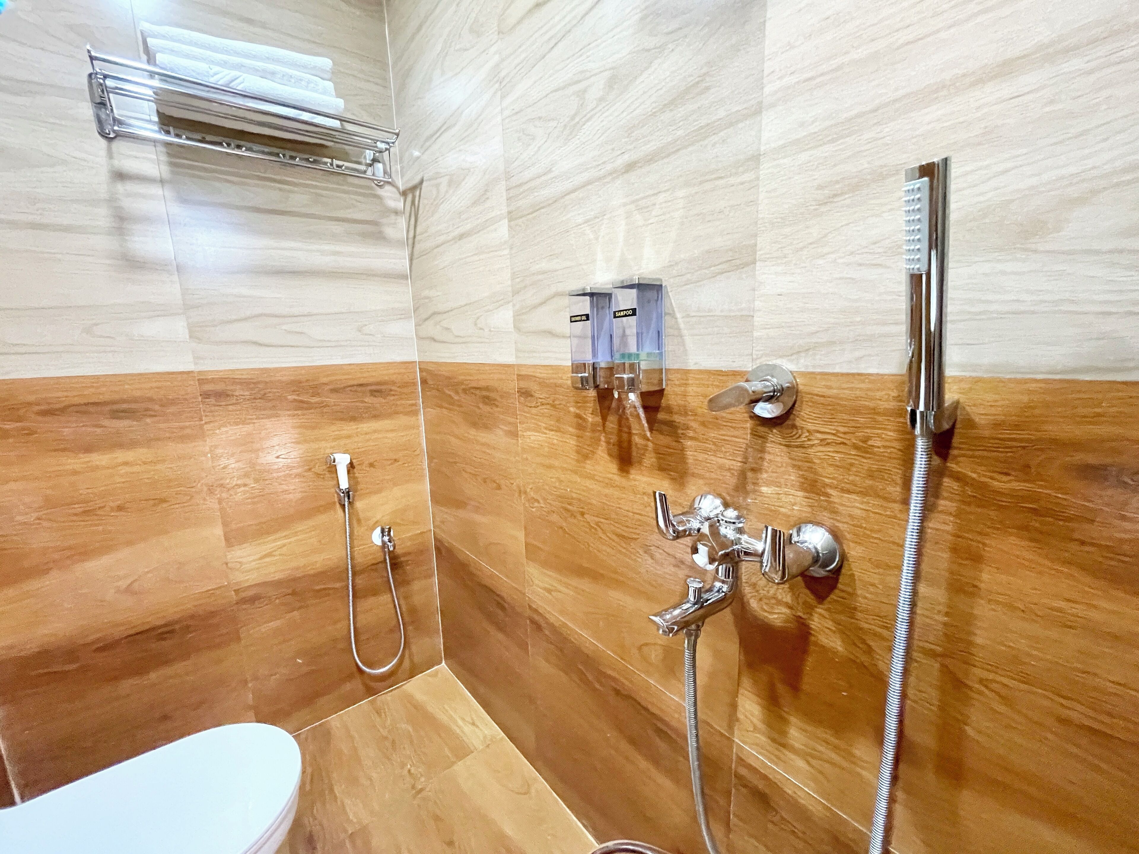A modern bathroom with a wooden floor, a glass shower enclosure, a toilet, and a sink with a handheld showerhead.