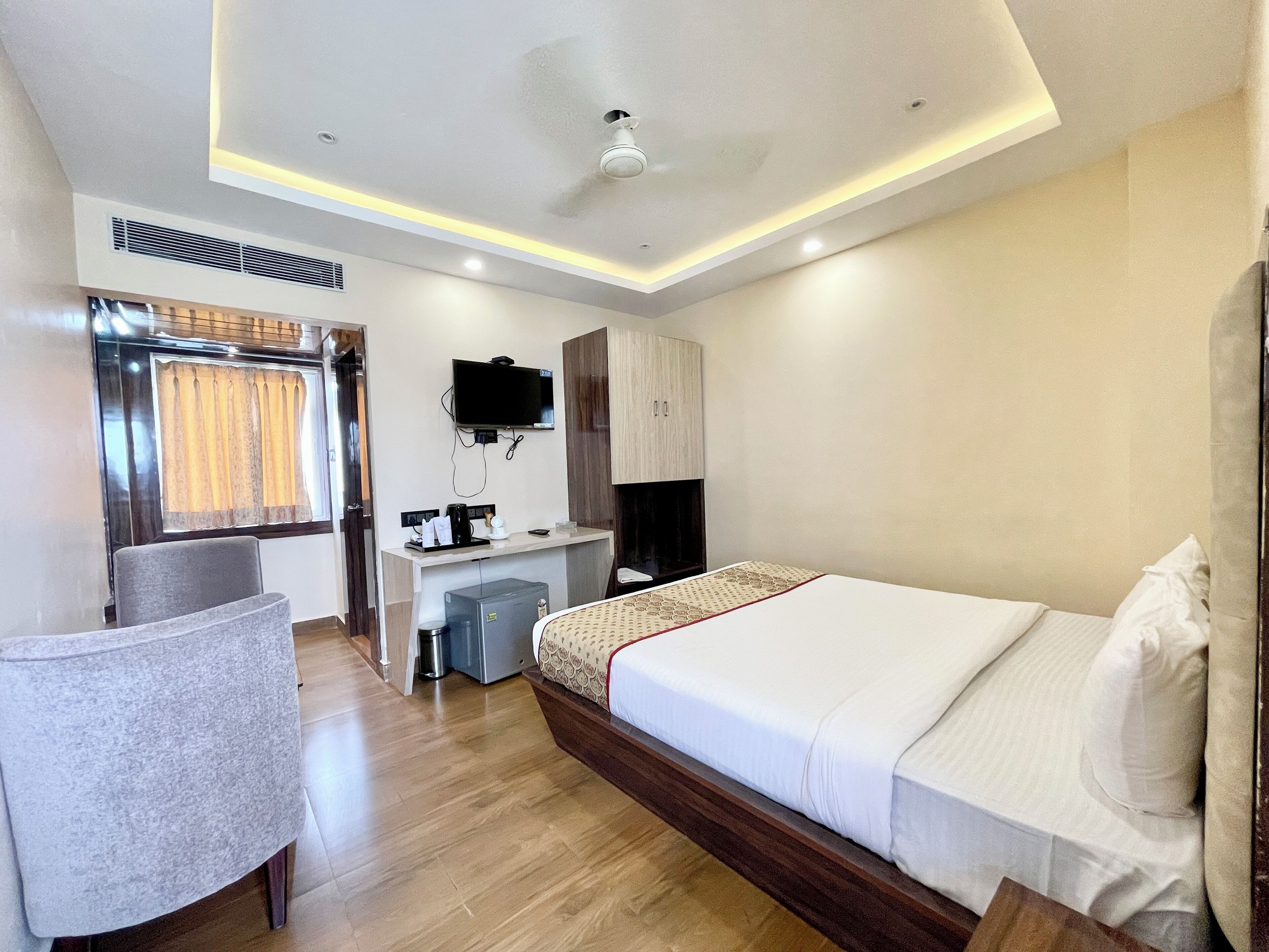A hotel room with a bed, a desk, a chair, a TV, and a window with curtains.