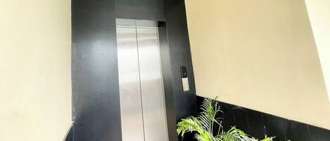 An elevator with a metallic finish, a wooden ceiling, and a potted plant beside it.