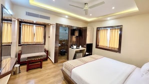 A hotel room with a bed, a seating area, a desk, and a ceiling fan. - A One Pride - Puri near Sea Beach (Puri)