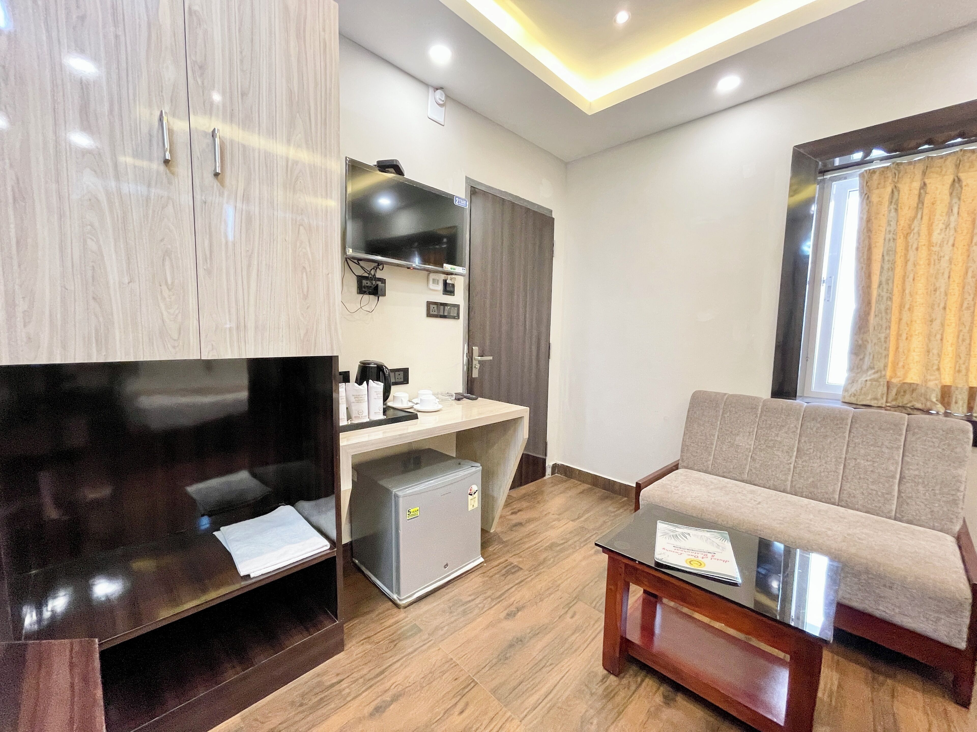 A modern living room with a flat-screen TV, a small kitchenette, a sofa, and a coffee table.