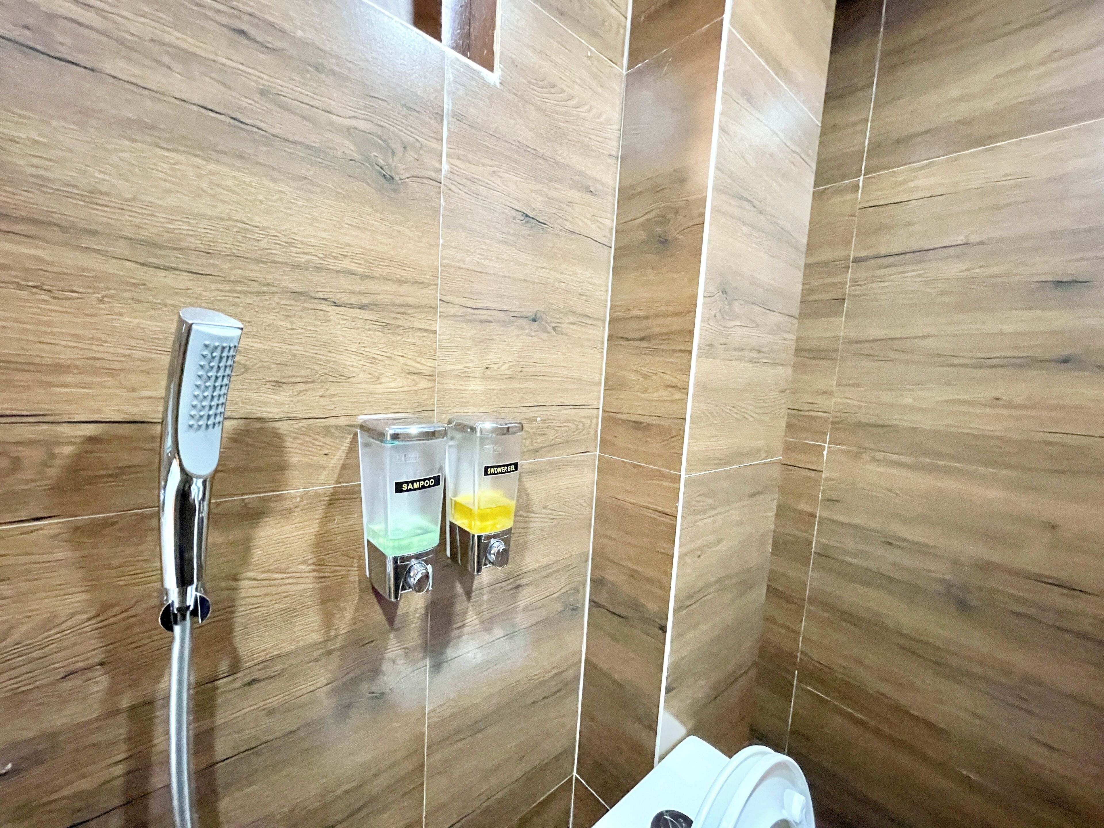 A shower area with a handheld showerhead, two shampoo bottles, and a shower gel bottle.