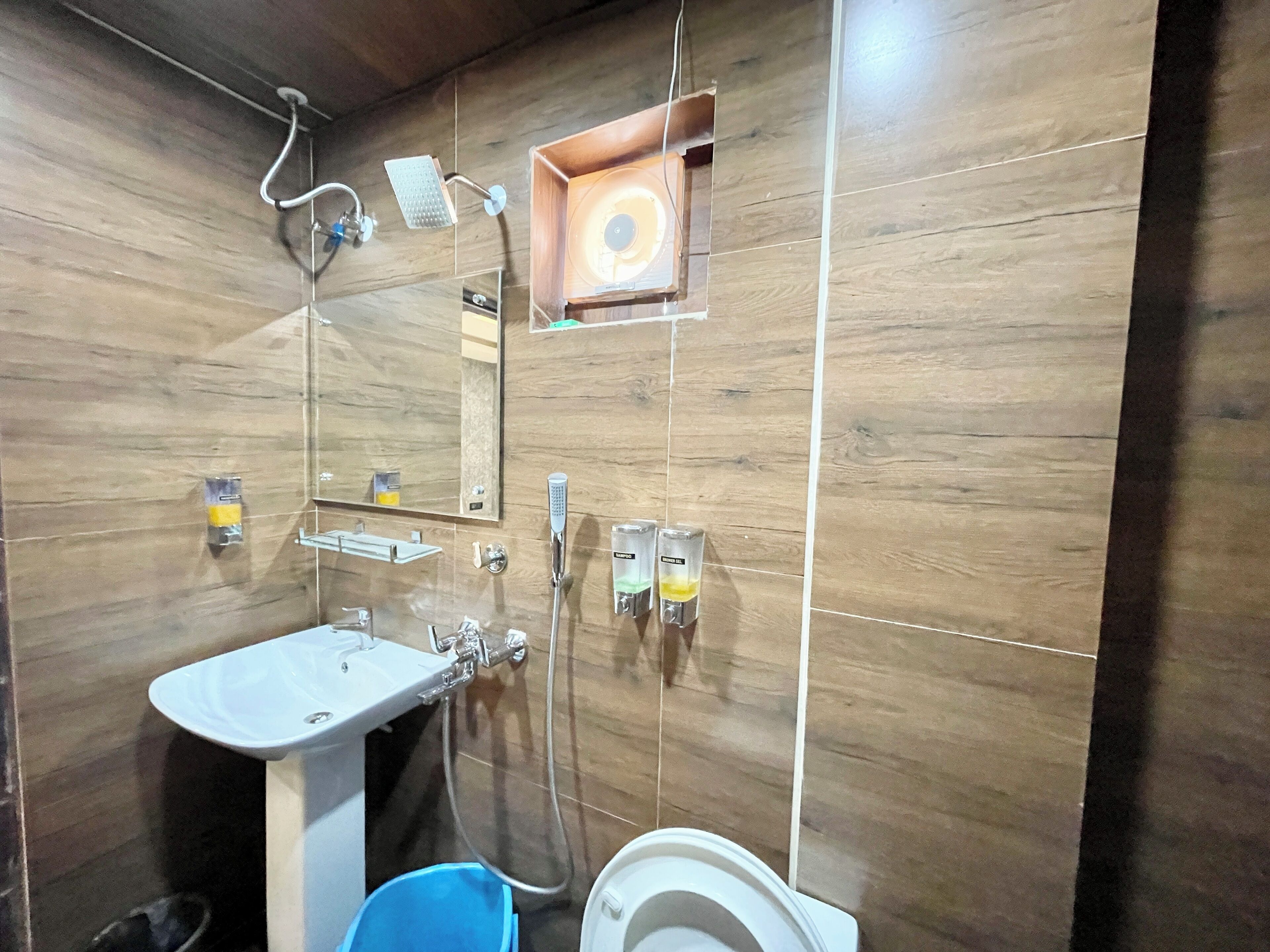 Un baño con pared de madera, un lavabo, un espejo, una ducha y un inodoro.