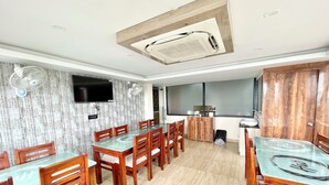 A dining area with a glass-top table, wooden chairs, a built-in air conditioning unit, a television mounted on the wall, and a wooden cabinet with a sink. - A One Pride - Puri near Sea Beach (Puri)