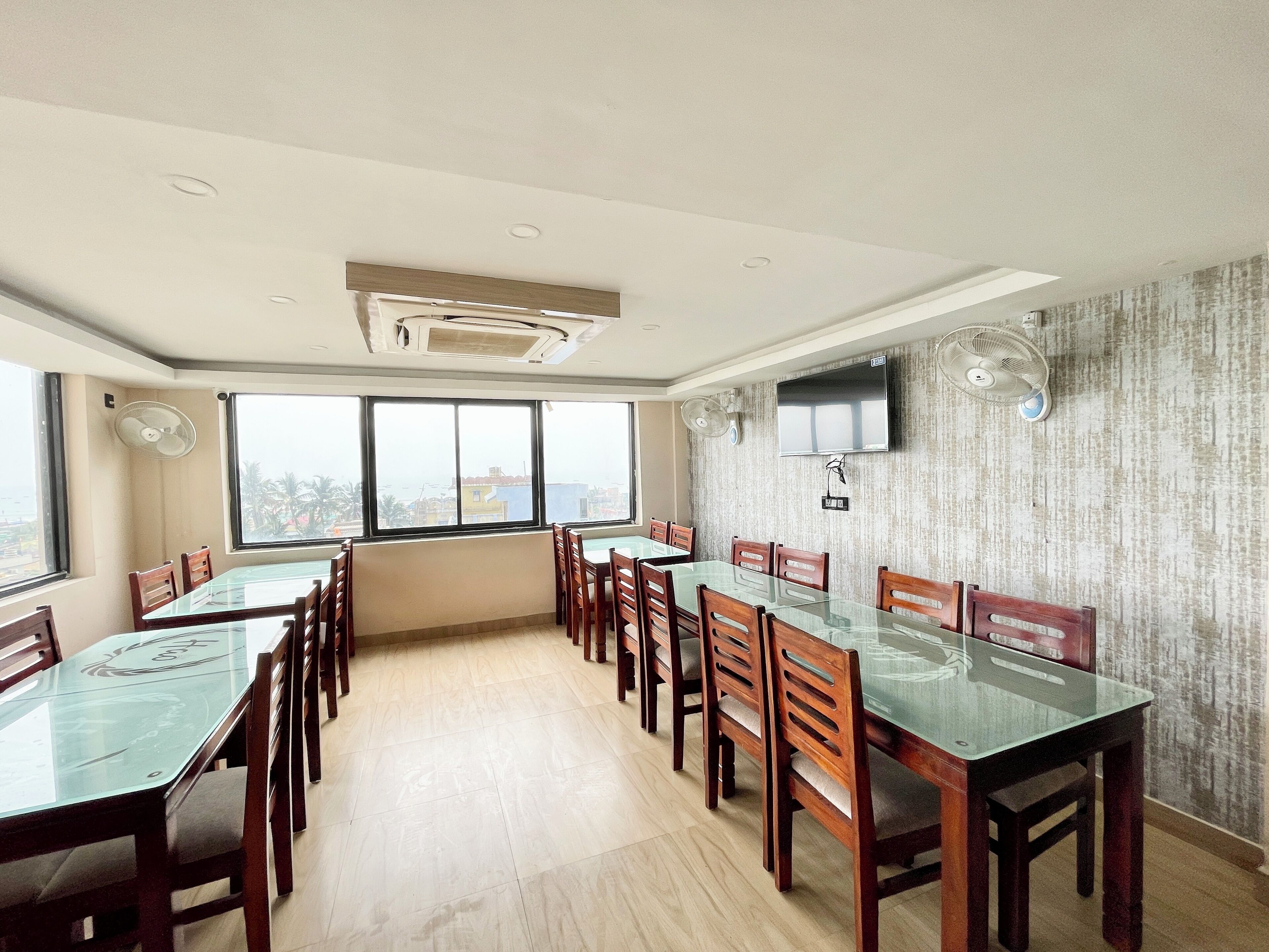 A spacious dining area with a high ceiling, large windows, and a flat-screen TV mounted on the wall.