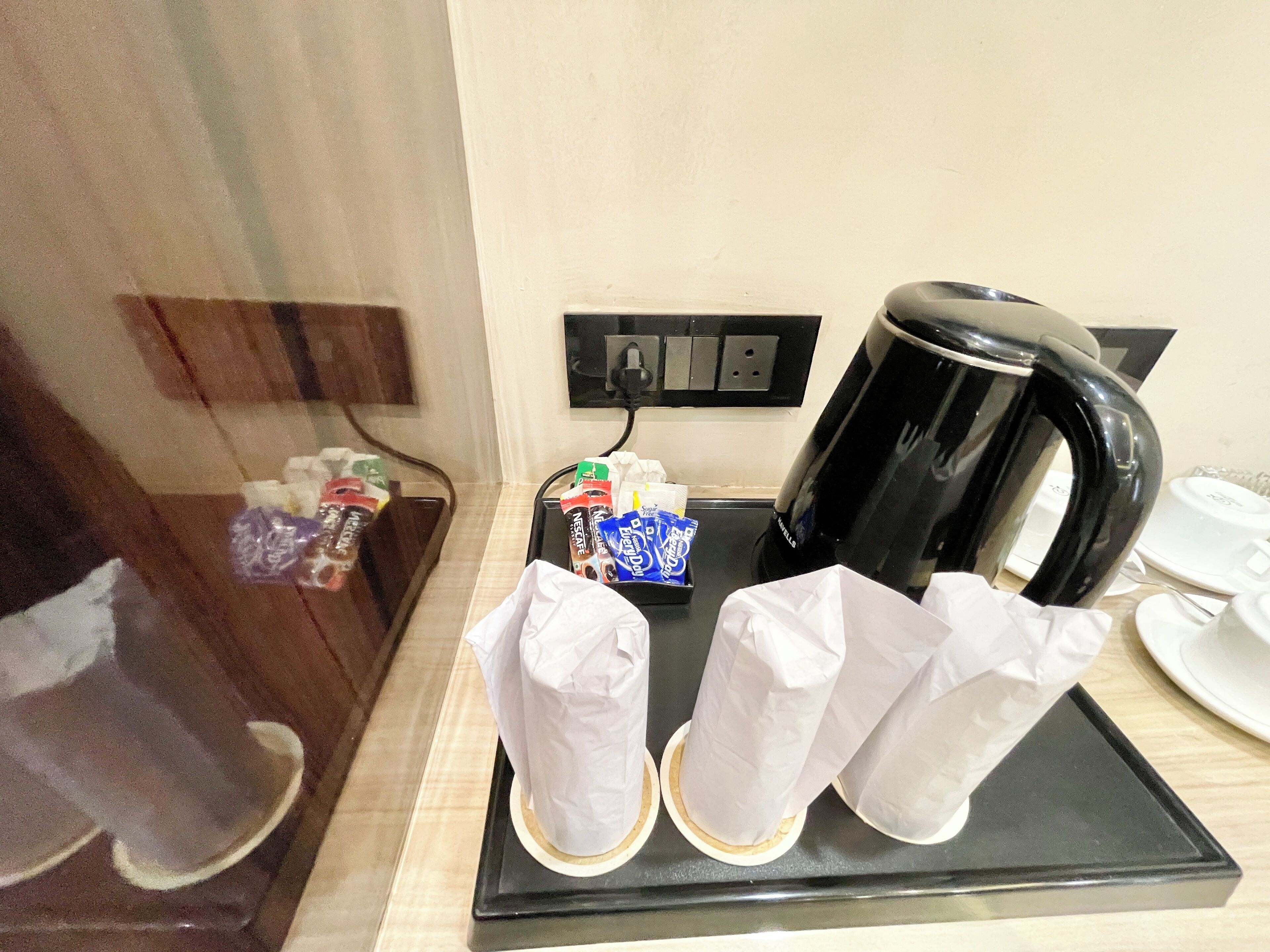 Una estación de café con una cafetera negra, vasos desechables y diferentes tipos de cápsulas de café.