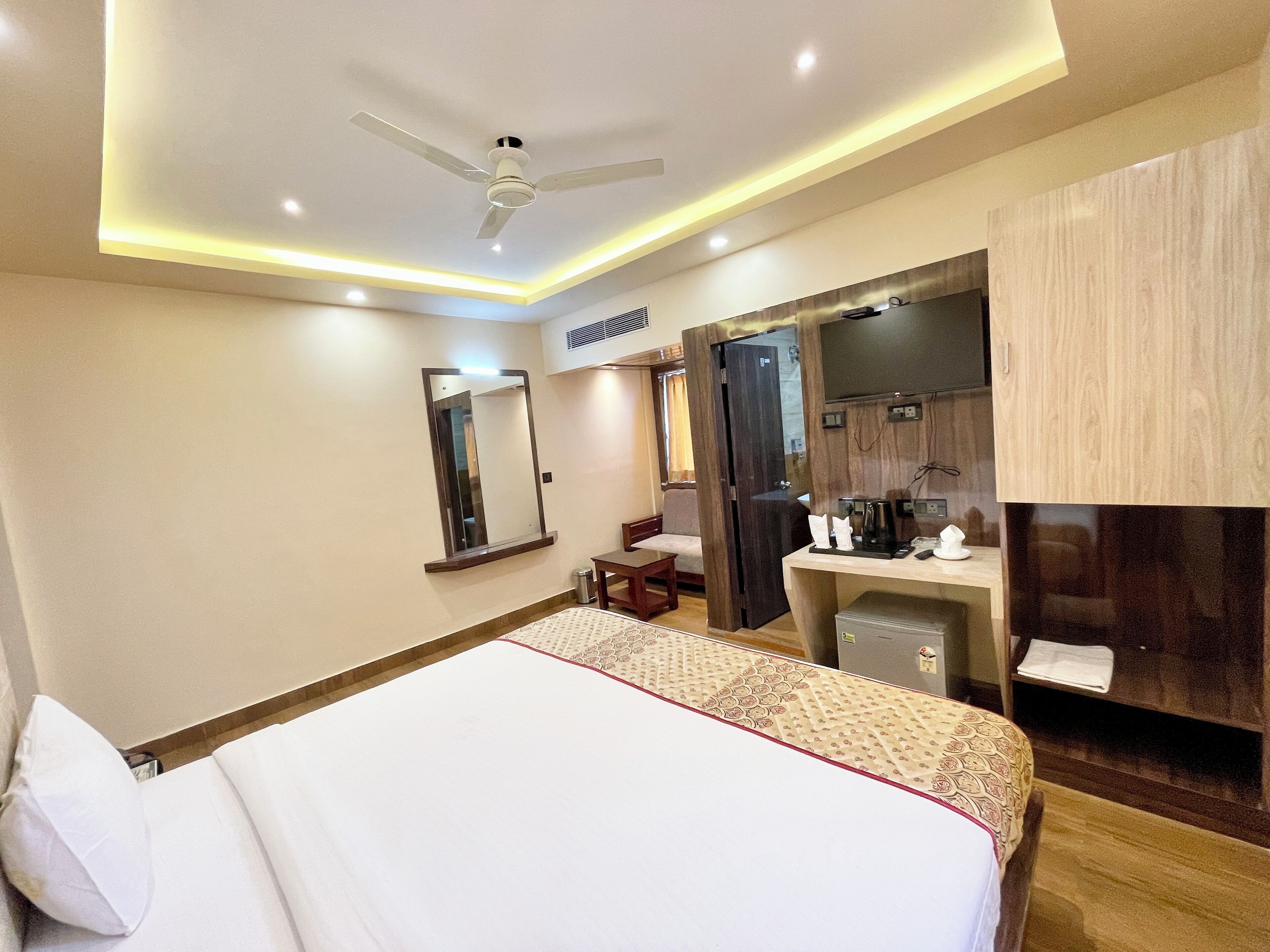 Ein Hotelzimmer mit Bett, Schreibtisch, Spiegel, Kleiderschrank und Deckenventilator.