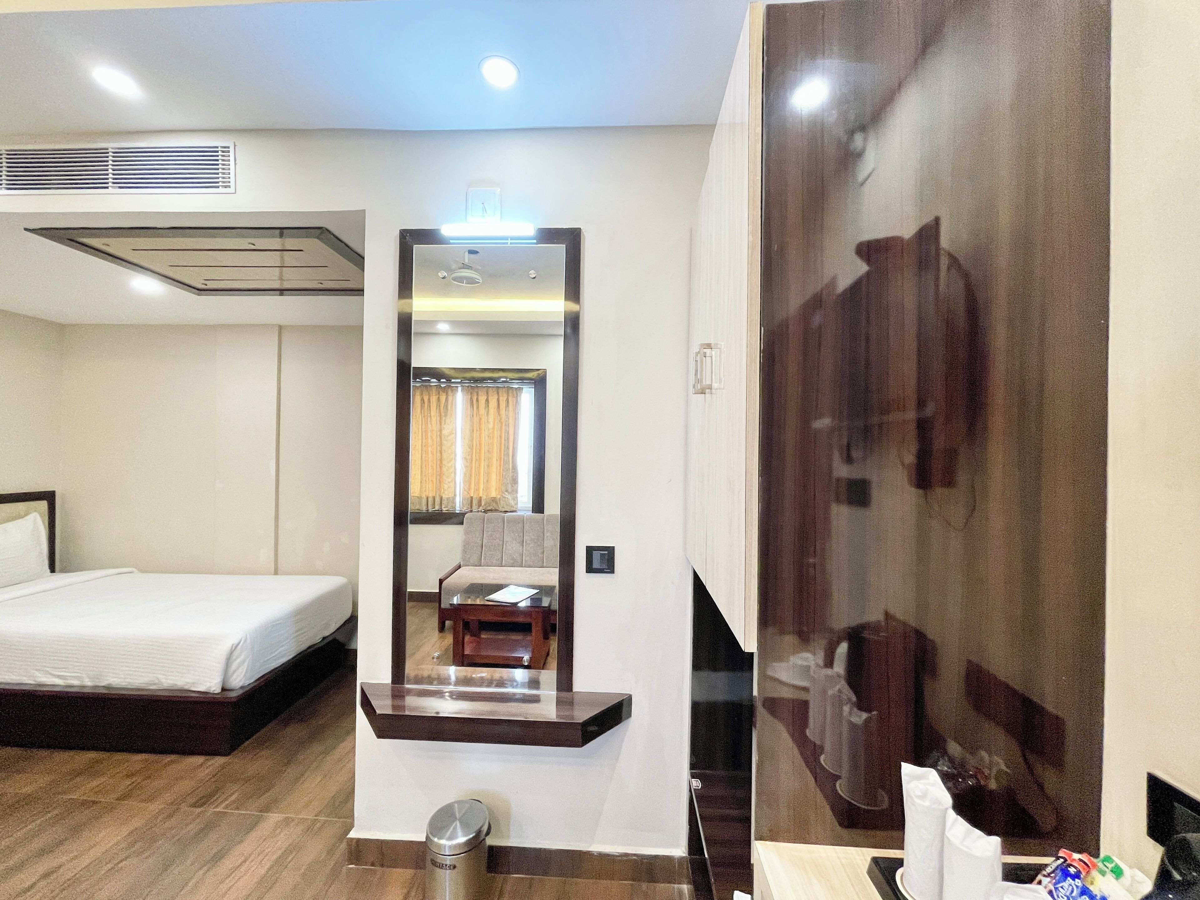 A hotel room with a bed, a mirror, a small table, and a trash bin.