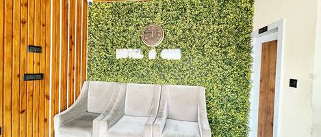 A reception area with a green wall, a clock, and a three-seater sofa.