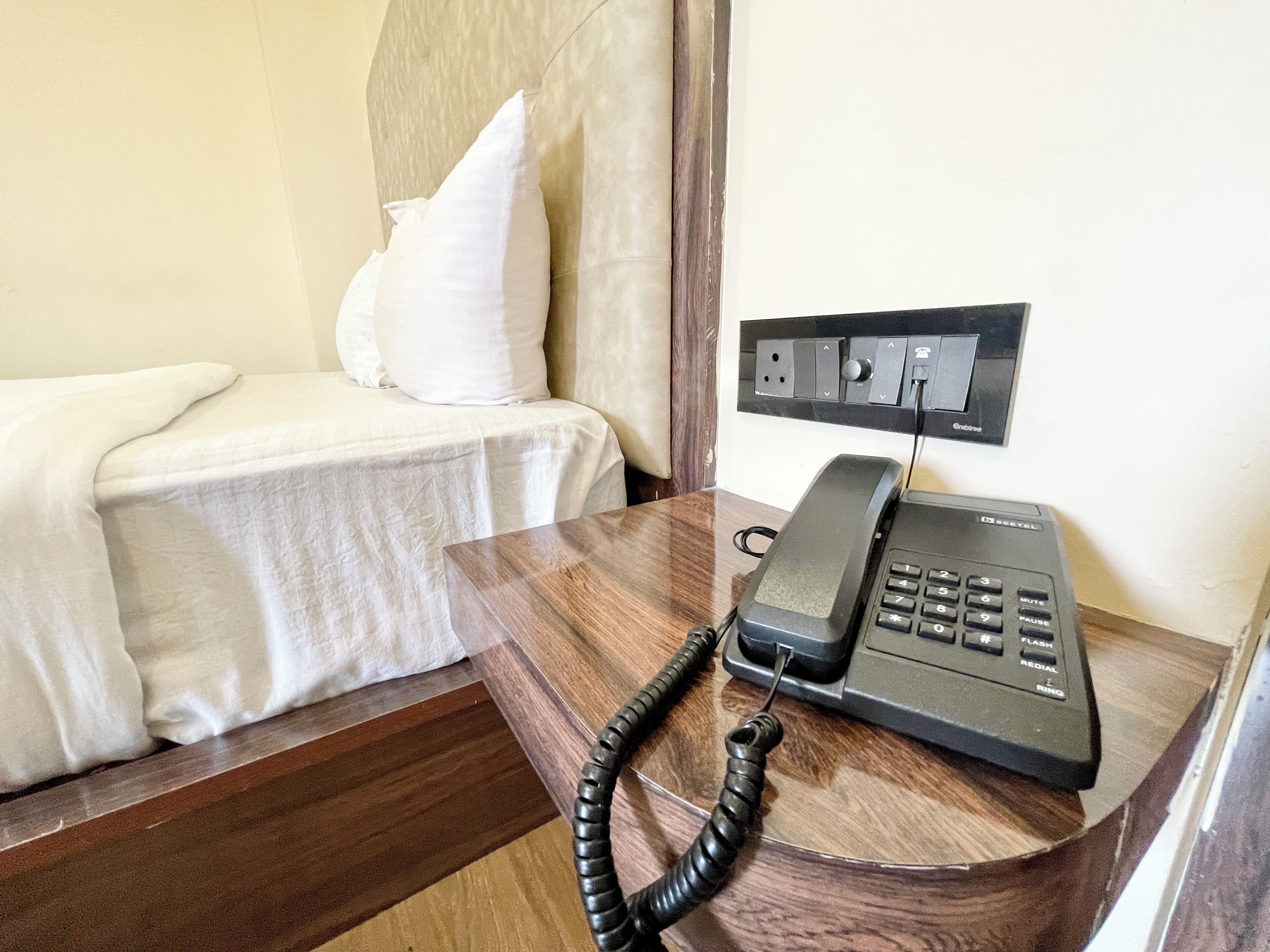Een houten nachtkastje met een zwarte telefoon en een stopcontact met stekker.