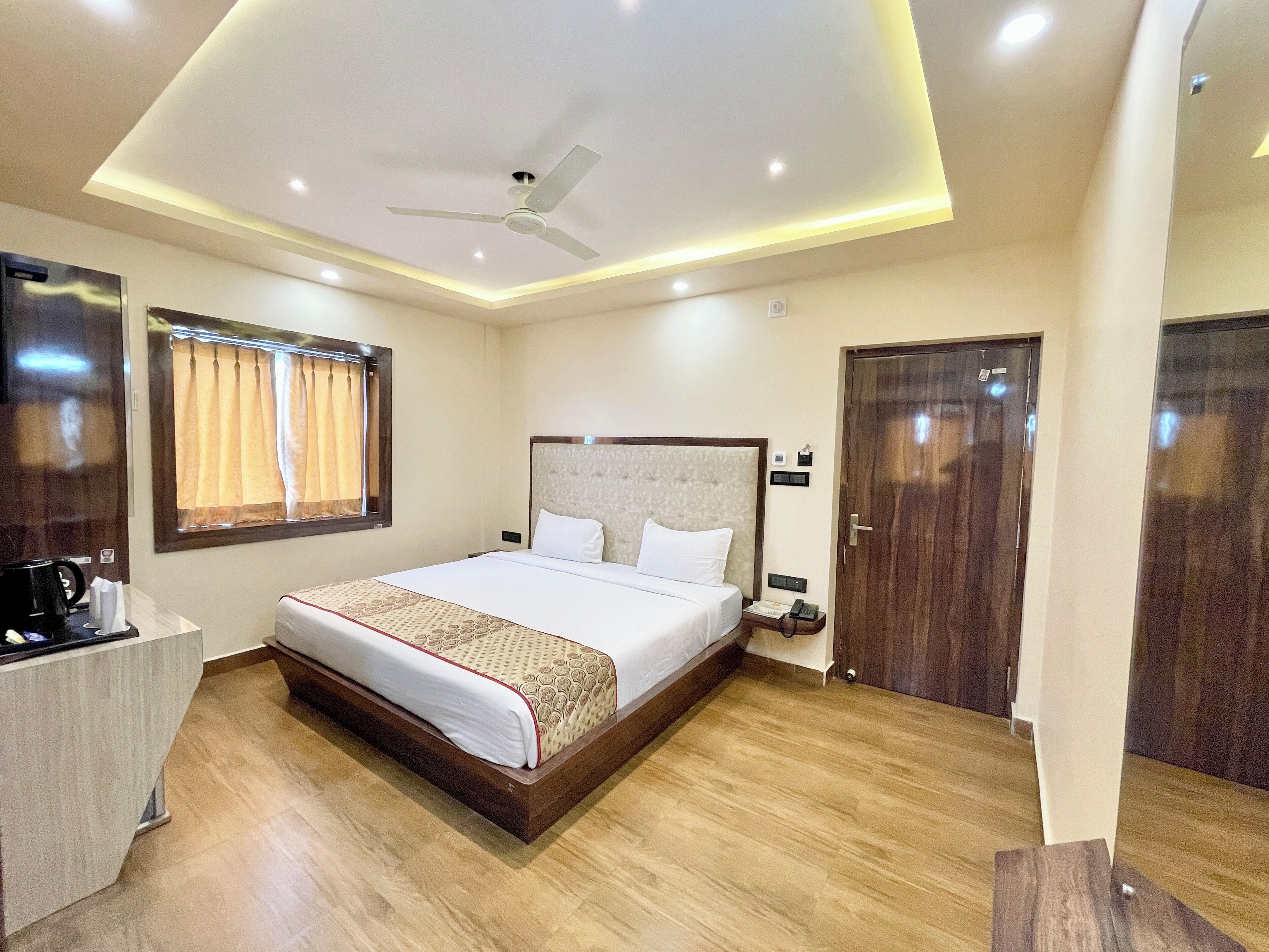Een hotelkamer met een groot bed, een nachtkastje met een telefoon, een plafondventilator en een raam met gordijnen.