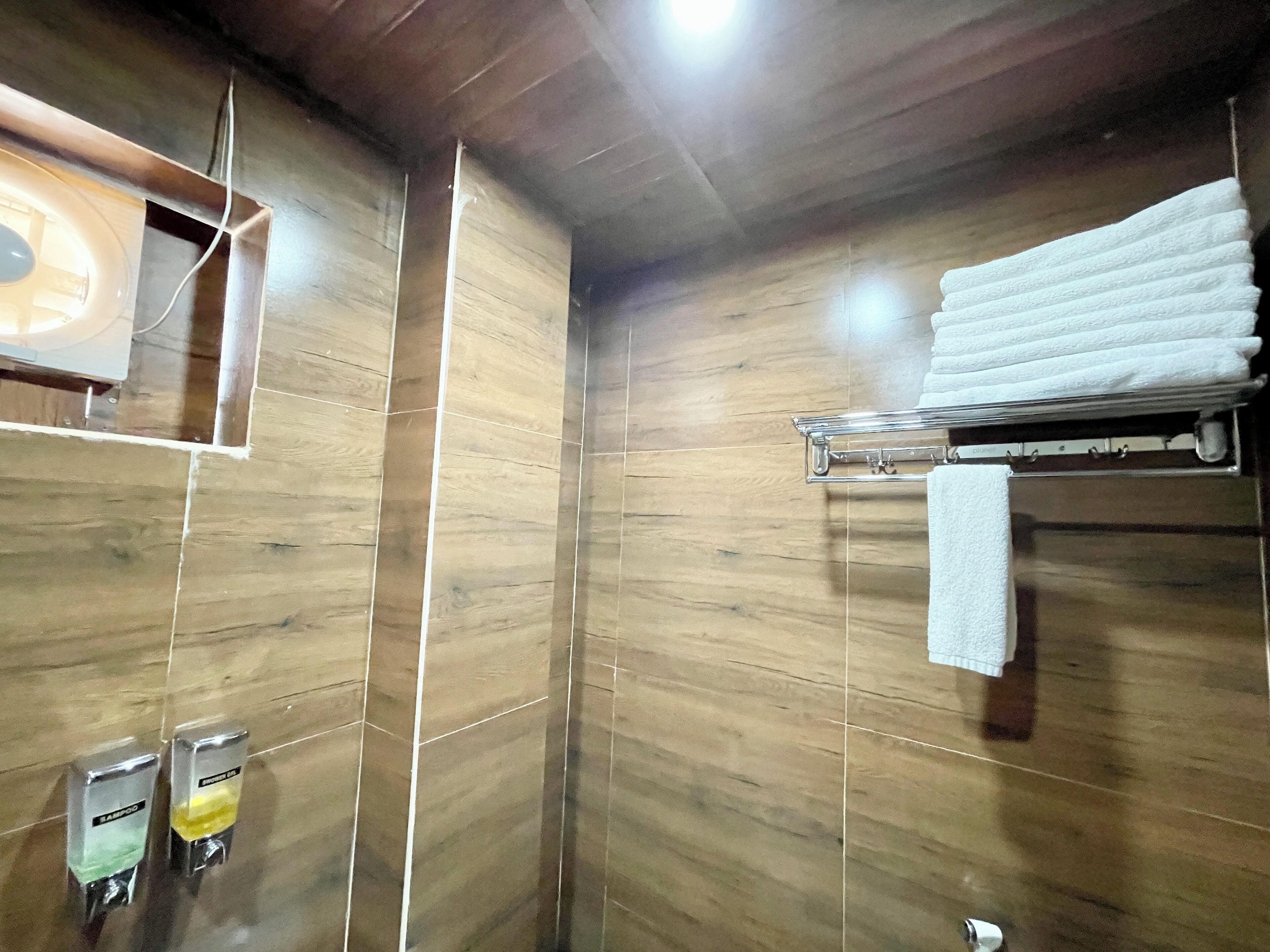 Un baño con paredes de madera, un perchero con toallas dobladas y dos dispensadores de jabón para manos.
