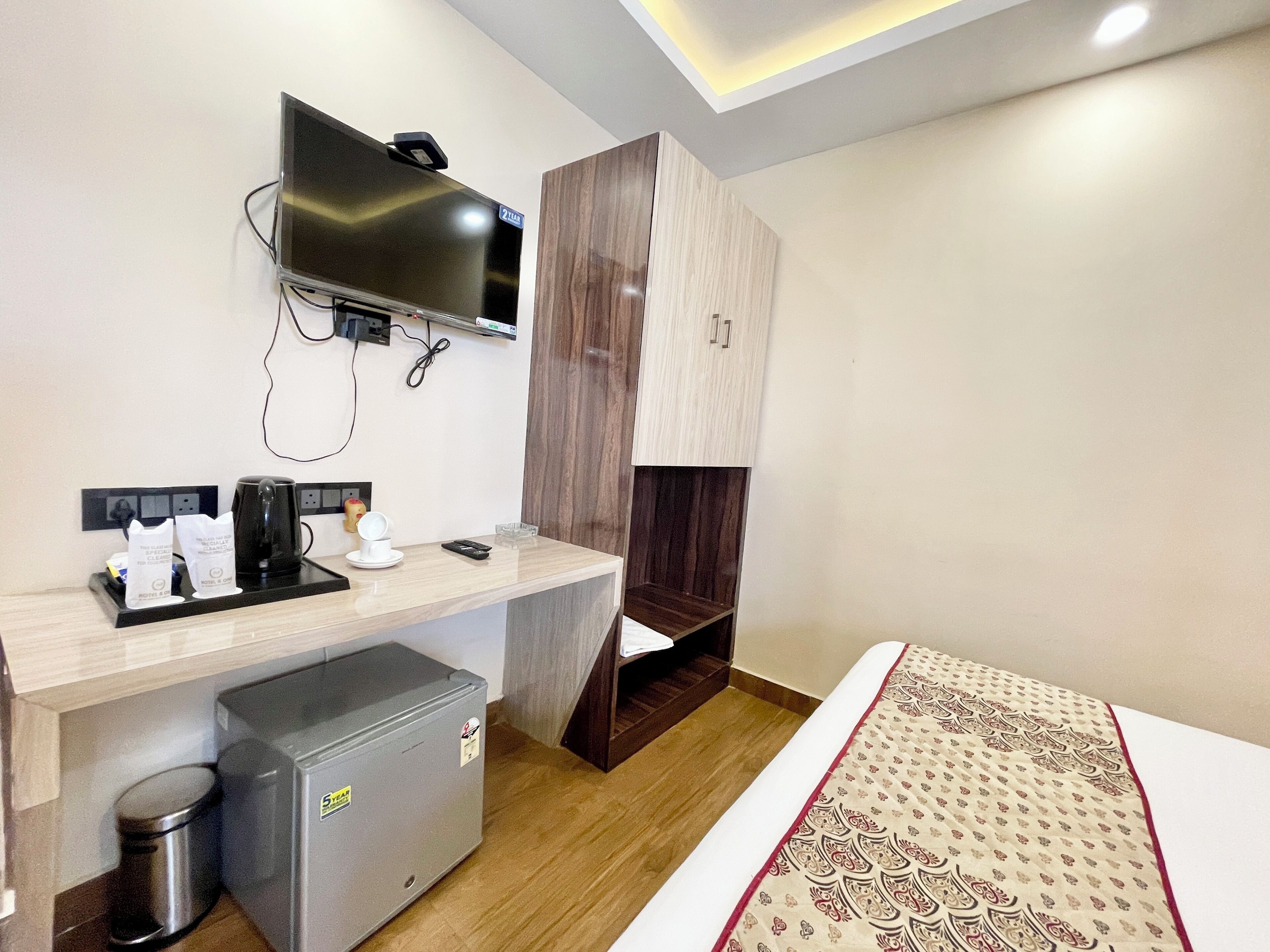A hotel room with a bed, a desk with a TV, a coffee maker, and a mini-fridge.