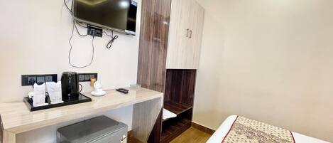 A hotel room with a bed, a desk with a TV, a coffee maker, and a mini-fridge.