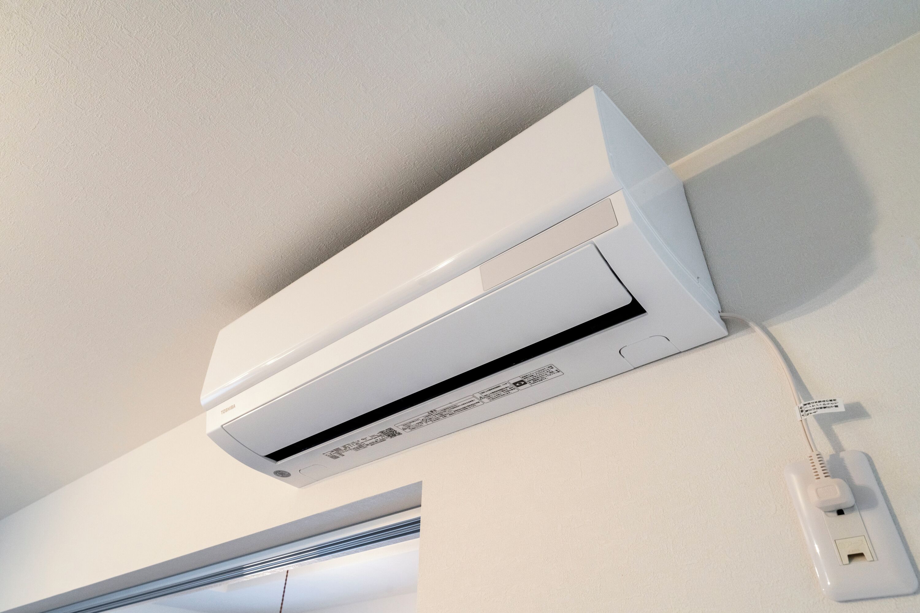 Un equipo de aire acondicionado blanco, fijado a la pared, con un cable de alimentación conectado a un enchufe.
