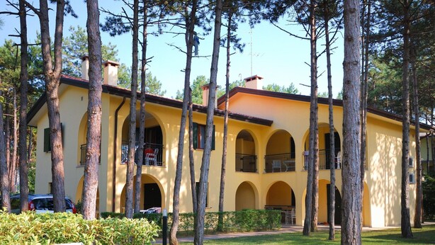 A yellow building with multiple balconies and a central courtyard surrounded by trees.