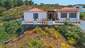 Une maison à deux étages, avec un toit en tuiles, un balcon et une vue sur une colline.