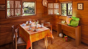 Ein Essbereich in einer Holzhütte mit einem Tisch für zwei Personen, einem Fenster mit Spitzenvorhängen und einem Hut an der Wand.