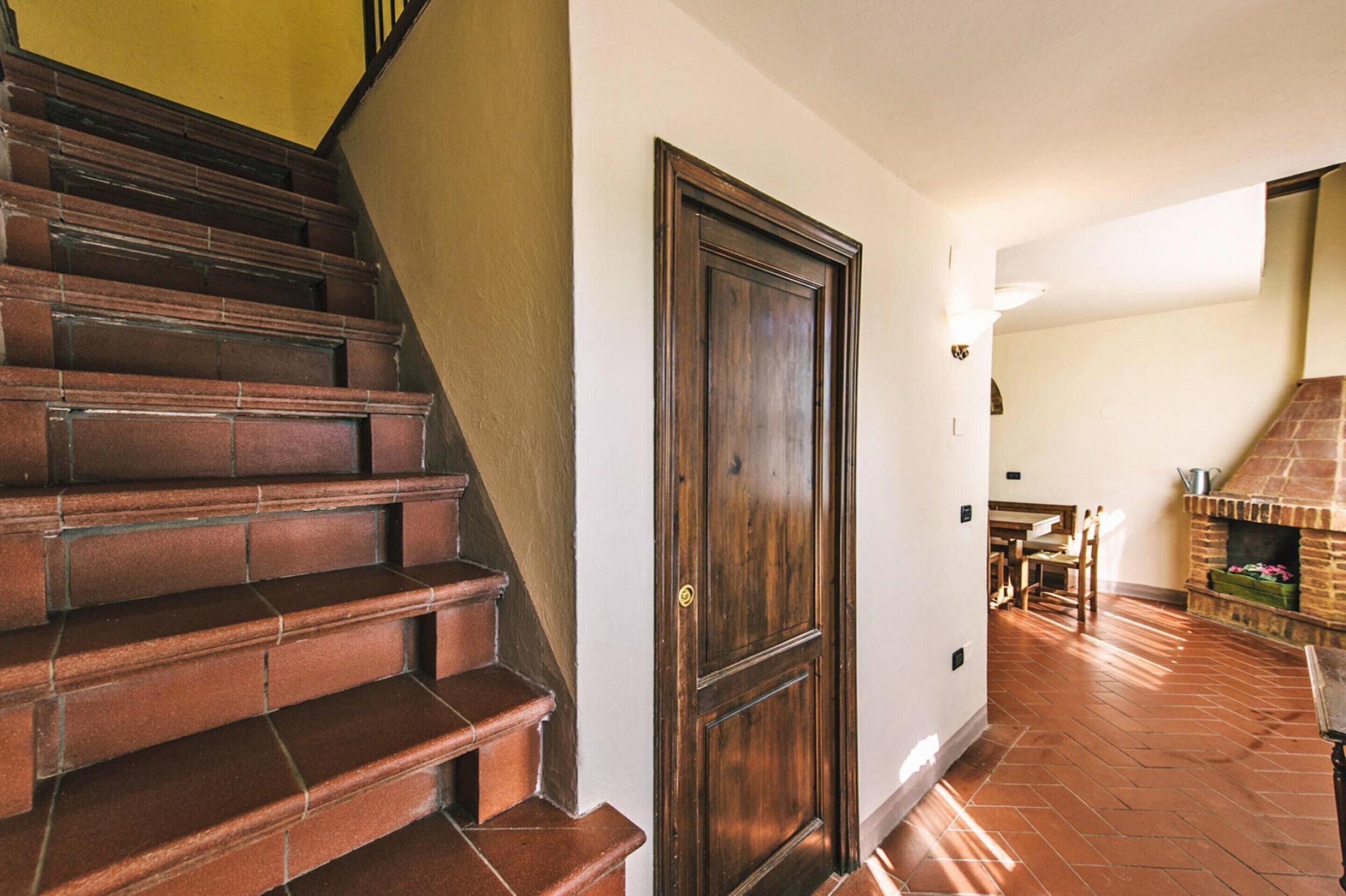 A staircase with wooden steps leading to a door, a brick fireplace, and a dining area with a table and chairs.